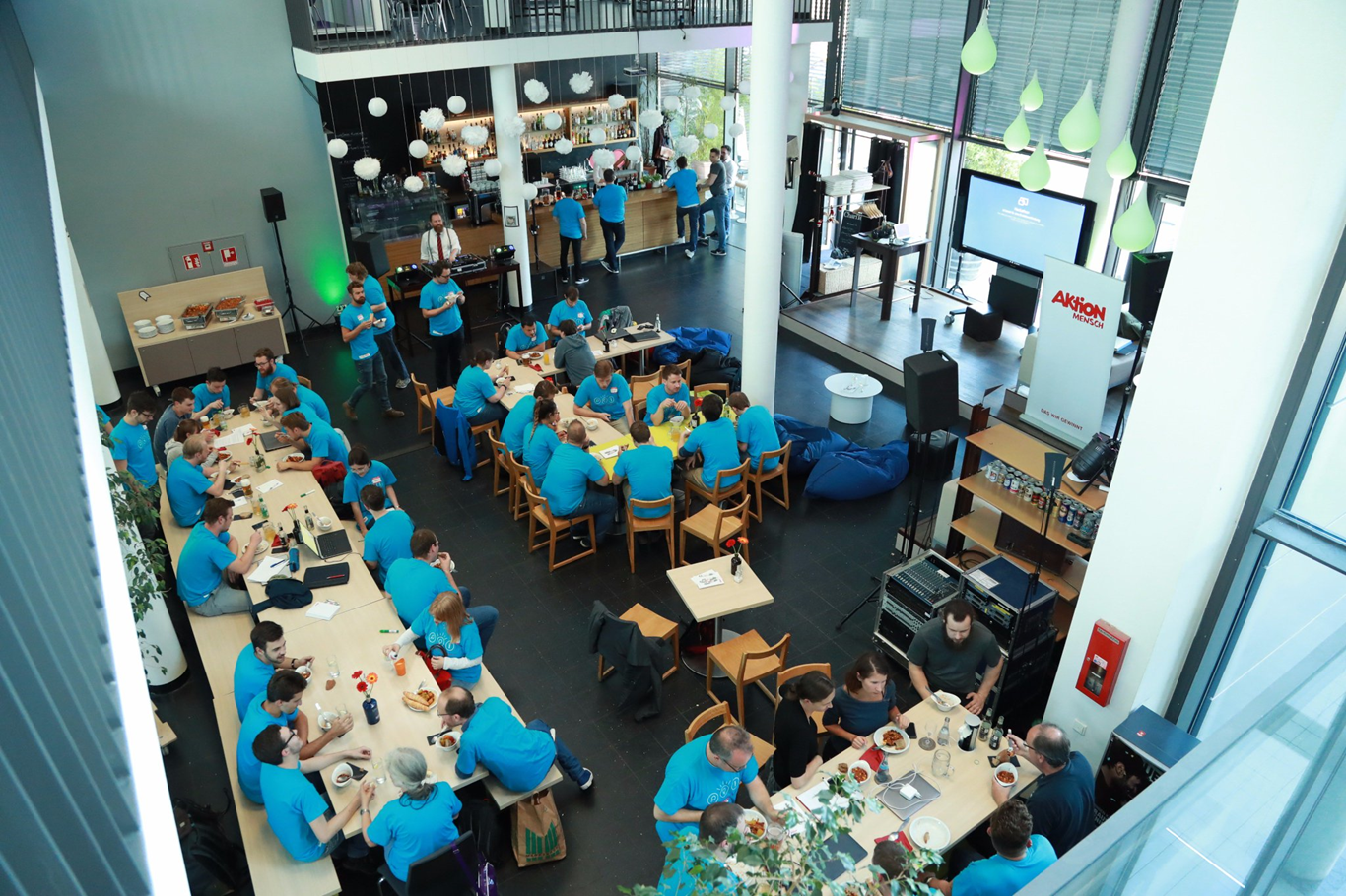 Aerial view of participants collaborating at the BIRNE7 hackathon event, seated at round tables in a large open hall